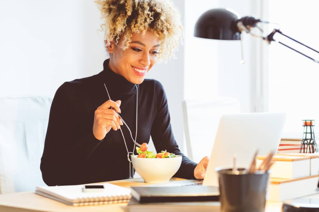 A woman eating a salad while working remotely. 